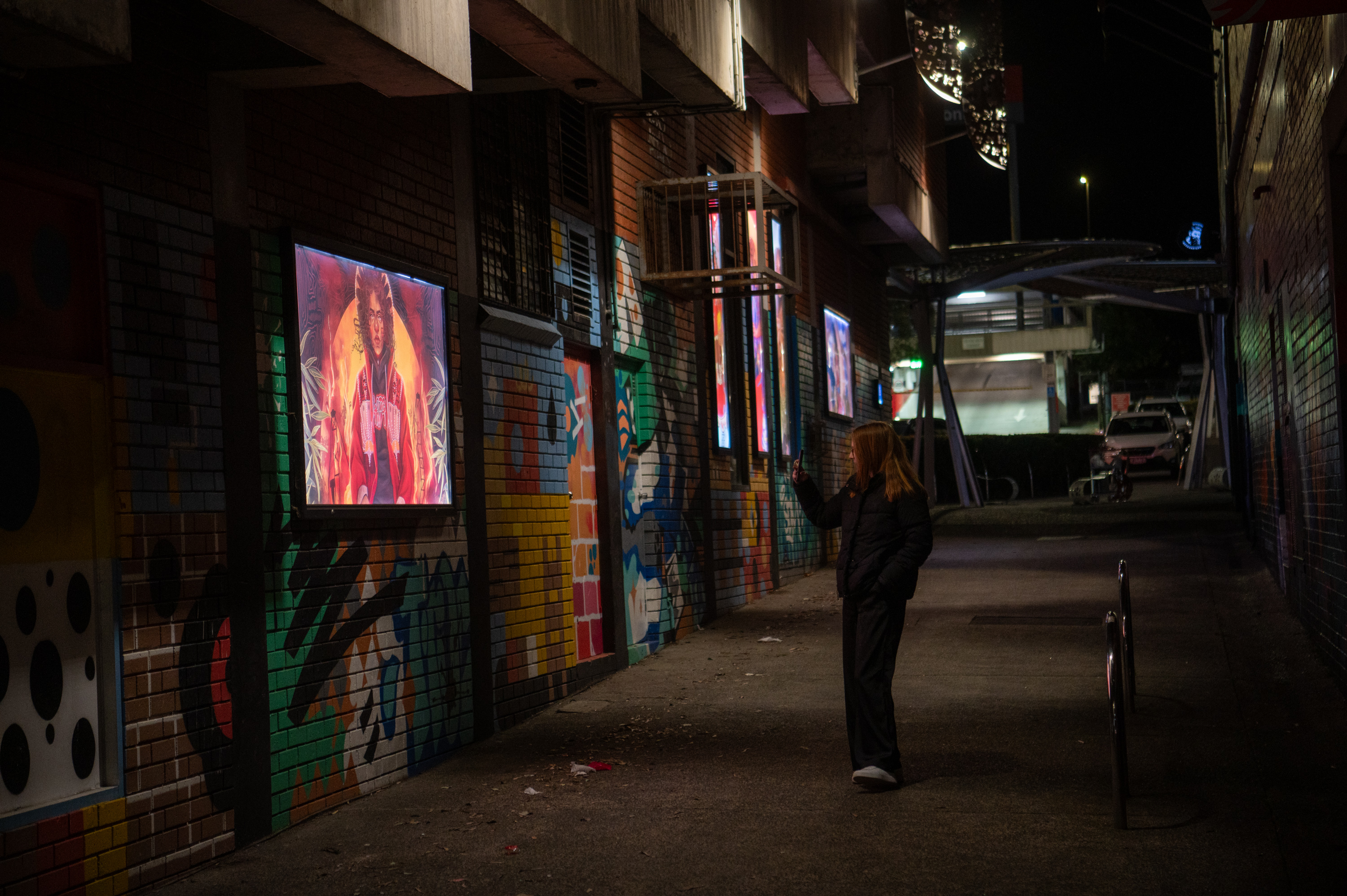 Lightboxes on the wall down an alleyway covered in graffiti