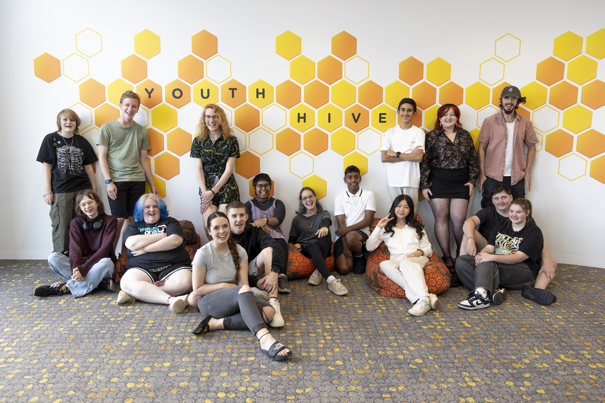 Young people sitting and standing in front of a wall with a honey comb pattern