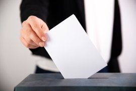 Person casting vote in ballot box.