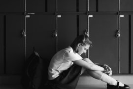 sad teenage girl sitting alone in front of school lockers