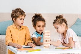 Three children at a table building a block tower 