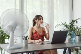 Women drinking water near a cooling fan. 