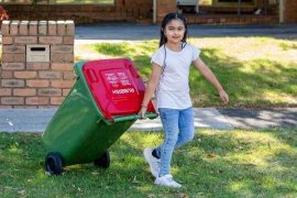 Young girl pulling red lidded rubbish bin out onto the street