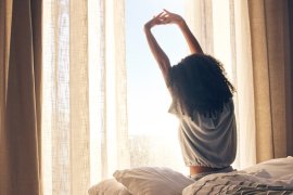 Female stretching while sitting on the bed as she wakes from sleep 