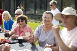 Group of people together around a table having morning tea.