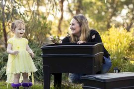 Mother and daughter in outdoor garden placing leaving into a home composting system