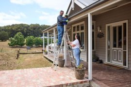 Two people clearing the gutter of their house ahead of fire season 