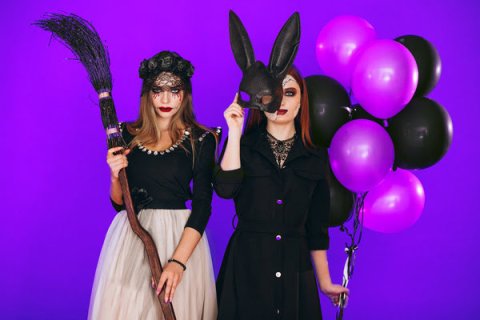 Two teenage girls in Halloween costumes in front of a purple background