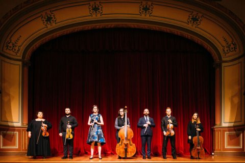 Seven musicians with various instruments on a stage