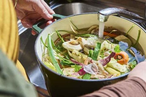 Image of person washing food scraps in a pan in a kitchen sink