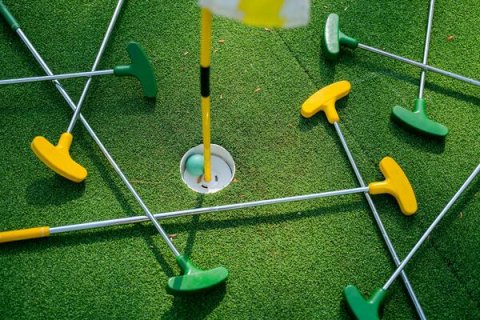 Green and yellow mini golf clubs, on a green with a mini golf hole