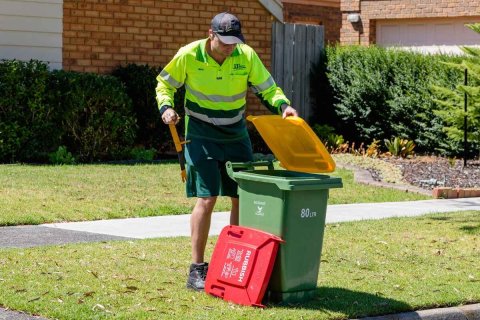 Male worker changing lid on residential rubbish bin from yellow to red