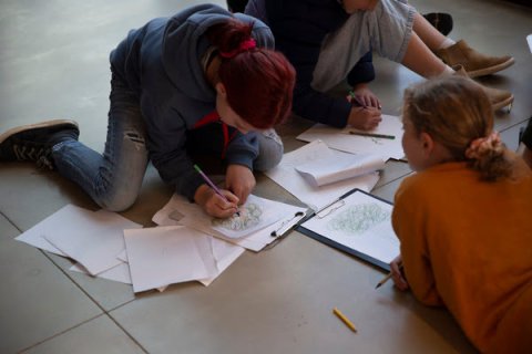 Young people sitting/ laying on tiled floor drawing artwork