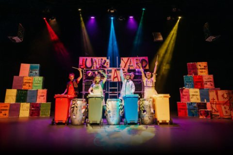 Four people on stage using garbage bins as drums