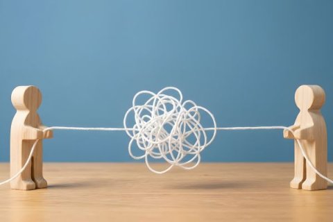 Two wooden figures pulling a tangled string, concept of resolving conflict untangling a problem and teamwork communication